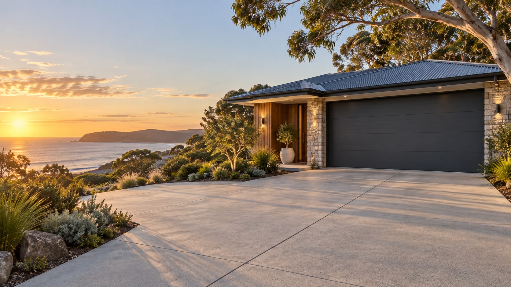 Modern coastal home with a broad concrete driveway, native landscaping and warm evening light